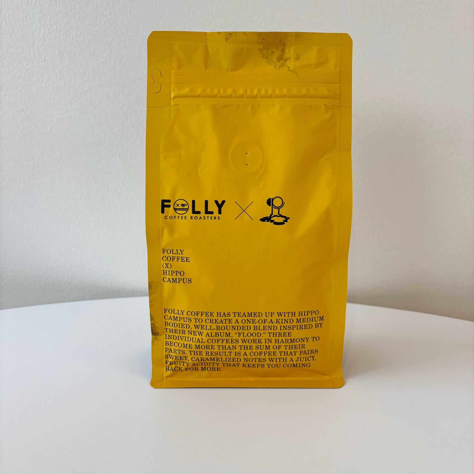Yellow bag of Folly Coffee x Hippo Campus medium-bodied blend with caramel and fruity tasting notes on white surface