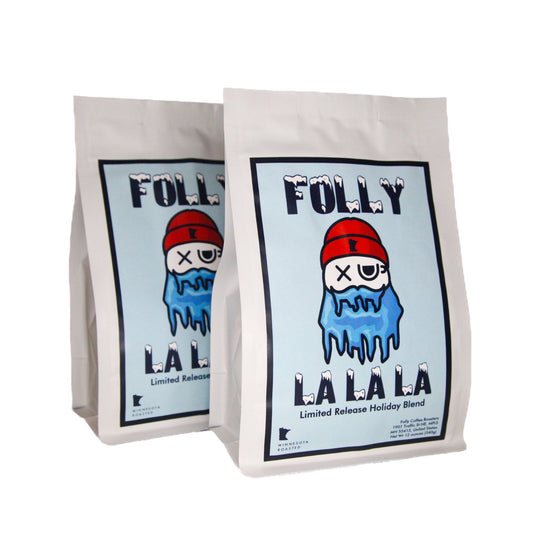 Two white bags with a cartoon icy figure wearing a red hat and text "Folly La La La Limited Release Holiday Blend" on light blue background